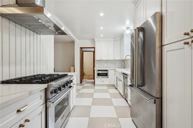 kitchen featuring backsplash, white cabinetry, stainless steel appliances, wall chimney range hood, and light floors