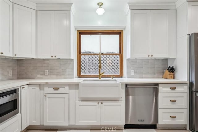 kitchen with appliances with stainless steel finishes, a sink, light countertops, and backsplash