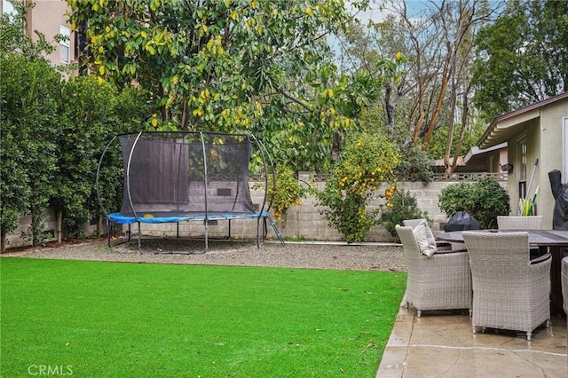 view of yard featuring a trampoline, a fenced backyard, outdoor dining space, and a patio area