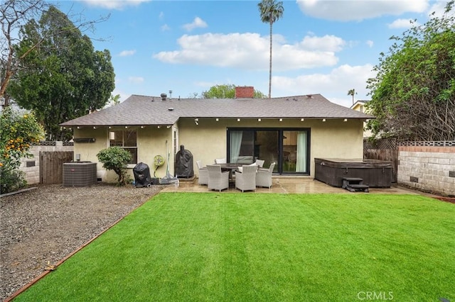 rear view of property featuring cooling unit, a fenced backyard, stucco siding, a hot tub, and a lawn