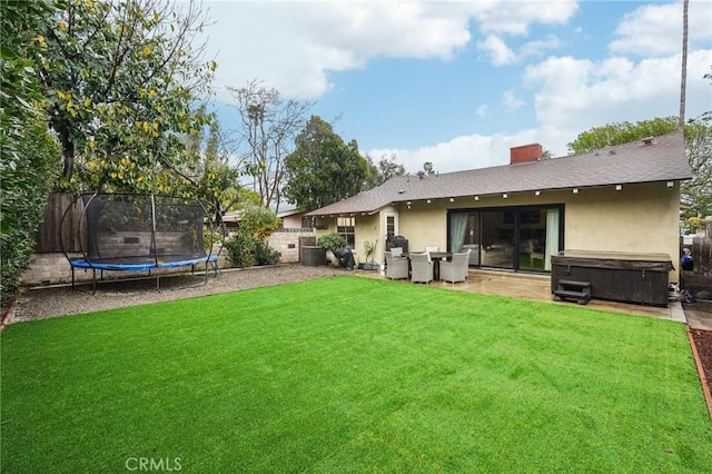 back of house featuring a yard, a fenced backyard, stucco siding, a hot tub, and a trampoline