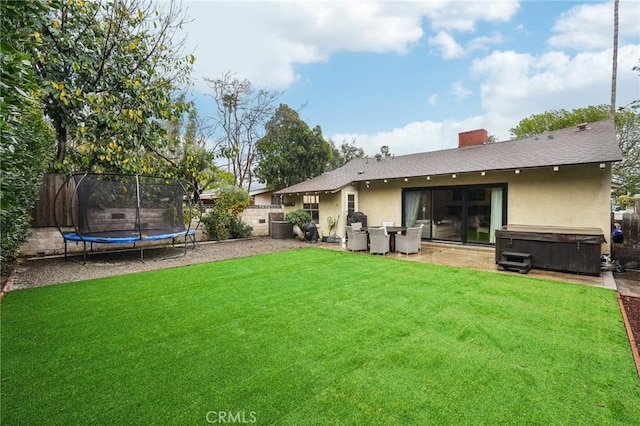 rear view of property featuring a trampoline, a fenced backyard, a lawn, a hot tub, and stucco siding
