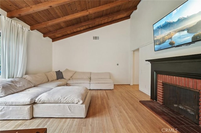 living area with vaulted ceiling with beams, wood finished floors, wood ceiling, a brick fireplace, and visible vents