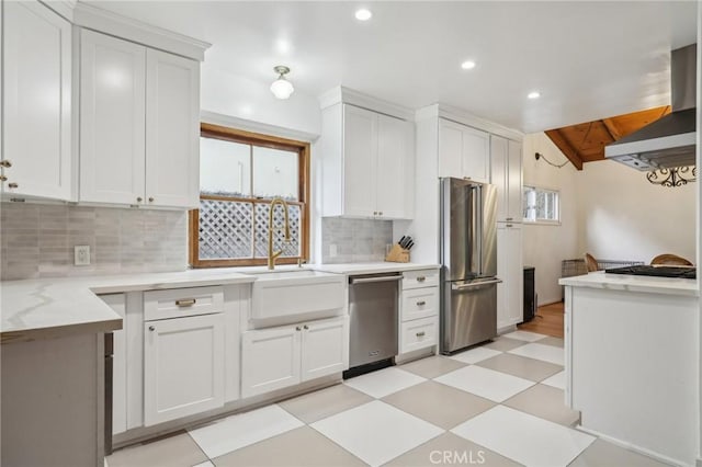 kitchen with stainless steel appliances, wall chimney range hood, white cabinets, backsplash, and a sink