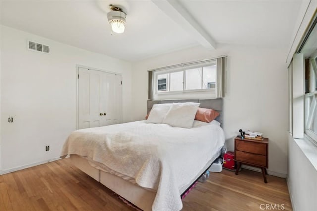 bedroom featuring wood finished floors, lofted ceiling with beams, a closet, baseboards, and visible vents