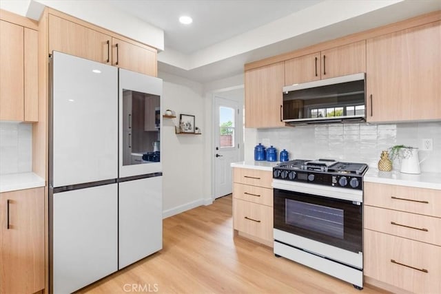 kitchen with gas range, light countertops, light brown cabinetry, and white fridge