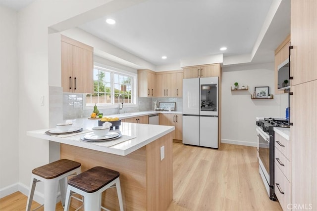 kitchen with light brown cabinetry, range with gas stovetop, a peninsula, and white refrigerator