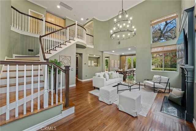 living room with baseboards, stairs, a high ceiling, an inviting chandelier, and wood finished floors