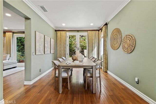 dining room featuring visible vents, wood finished floors, baseboards, and ornamental molding