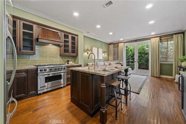 kitchen with hardwood / wood-style floors, visible vents, custom exhaust hood, a sink, and appliances with stainless steel finishes