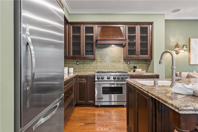 kitchen with premium range hood, appliances with stainless steel finishes, ornamental molding, and a sink