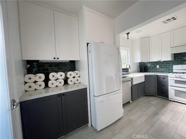 kitchen with white appliances, visible vents, a sink, white cabinetry, and tasteful backsplash