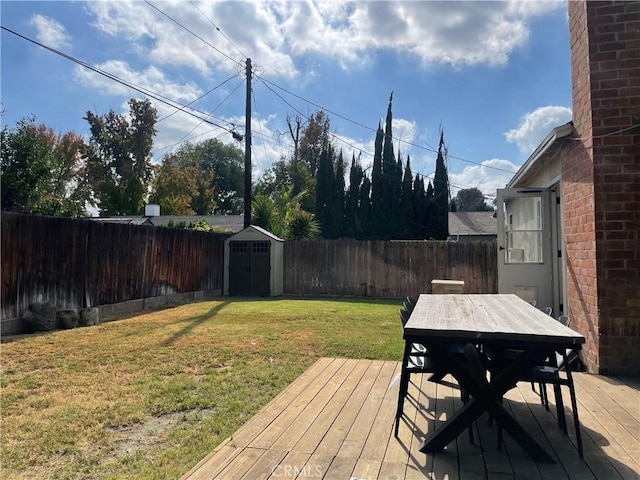 deck featuring outdoor dining space, an outbuilding, a fenced backyard, a storage unit, and a lawn