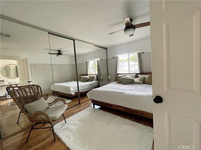 bedroom featuring visible vents, wood finished floors, a closet, wainscoting, and ceiling fan