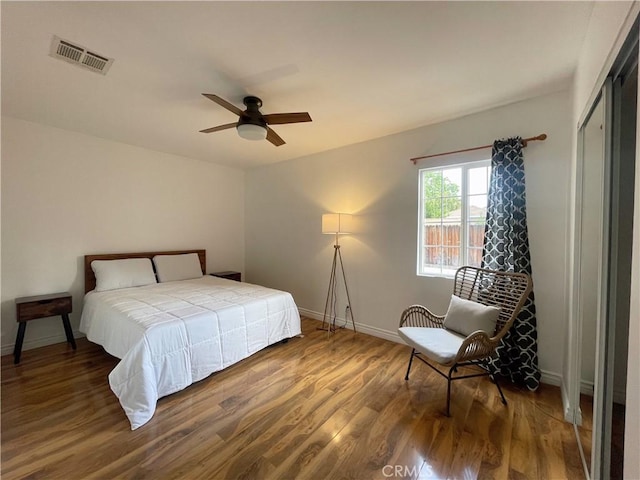 bedroom with ceiling fan, wood finished floors, visible vents, and baseboards