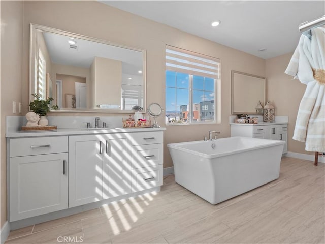 bathroom featuring wood finish floors, a freestanding tub, recessed lighting, baseboards, and vanity