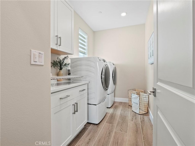 laundry room featuring light wood-style flooring, cabinet space, baseboards, and washer and clothes dryer