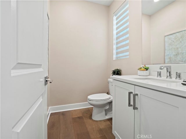 half bathroom featuring vanity, toilet, wood finished floors, and baseboards