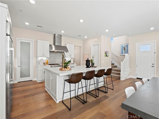 kitchen with visible vents, a kitchen bar, wall chimney range hood, tasteful backsplash, and light wood finished floors