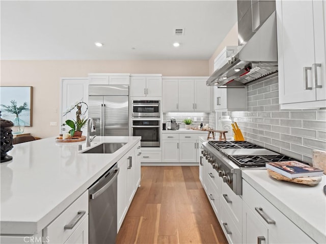 kitchen featuring a sink, wall chimney range hood, white cabinetry, stainless steel appliances, and light countertops