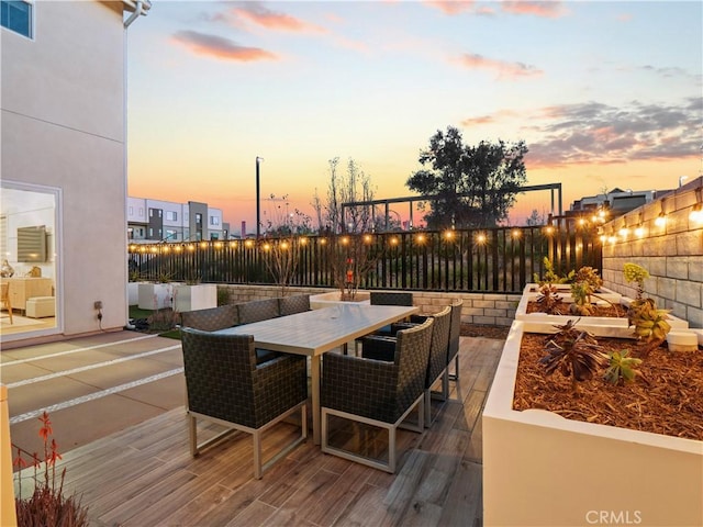 patio terrace at dusk with outdoor dining area, visible vents, and a fenced backyard