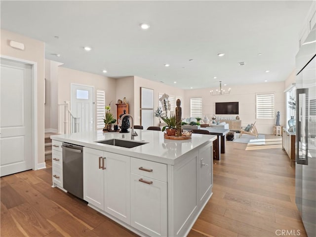 kitchen with white cabinetry, light wood finished floors, a kitchen island with sink, a sink, and stainless steel dishwasher