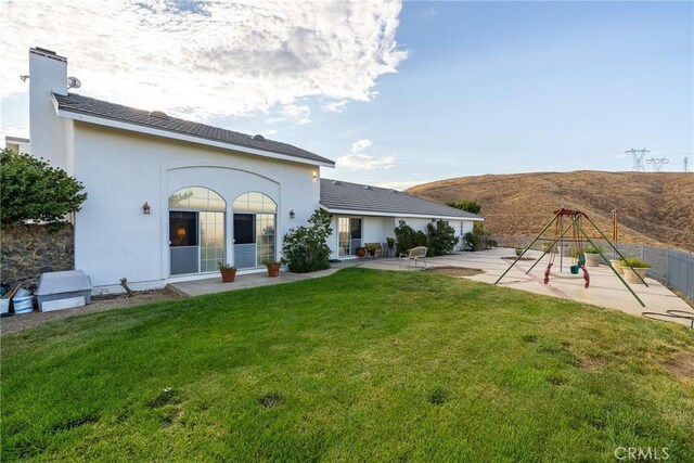 rear view of property with stucco siding, a lawn, a patio, fence, and a playground