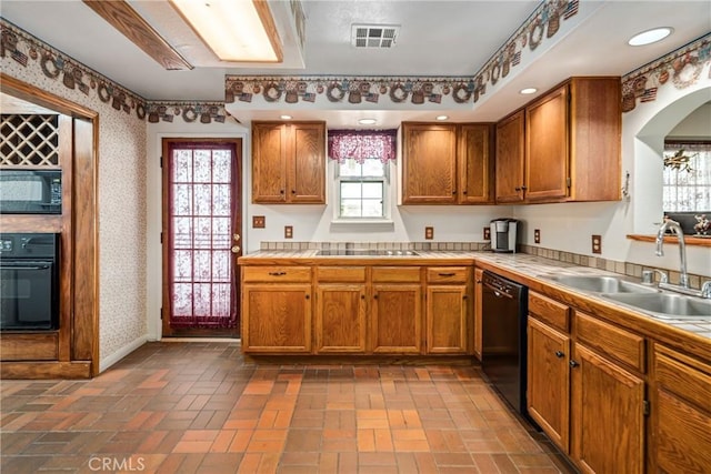 kitchen with tile countertops, black appliances, wallpapered walls, and a sink