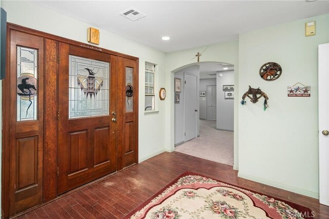 foyer entrance with wood finished floors, arched walkways, visible vents, and baseboards