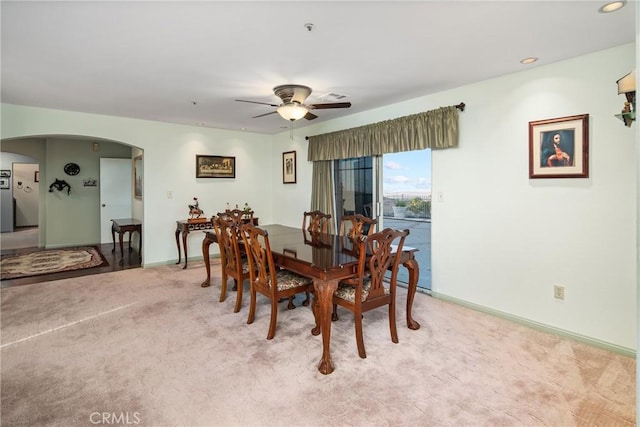 dining room with baseboards, arched walkways, light carpet, and a ceiling fan