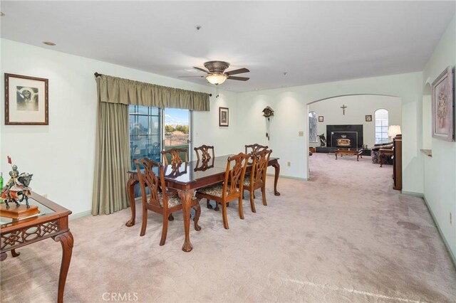 dining area with arched walkways, light colored carpet, baseboards, and a ceiling fan