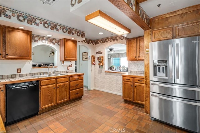 kitchen featuring wallpapered walls, a sink, tile counters, dishwasher, and stainless steel fridge