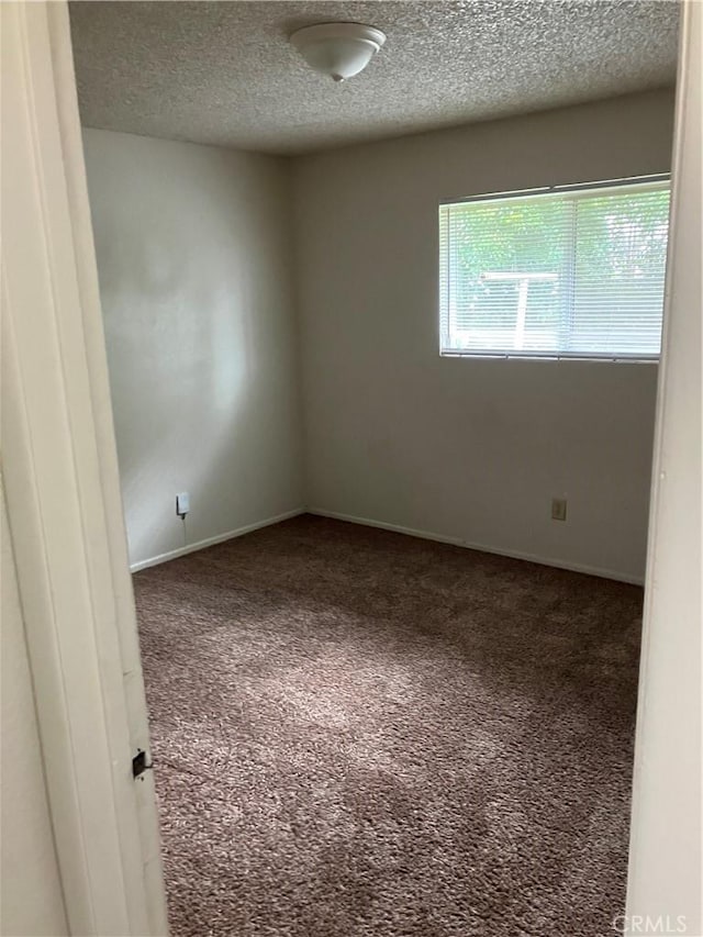 carpeted spare room featuring baseboards and a textured ceiling