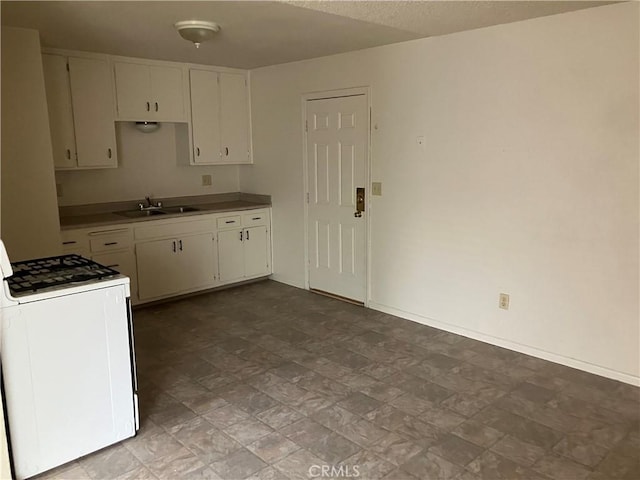 kitchen featuring white gas stove, white cabinets, baseboards, and a sink