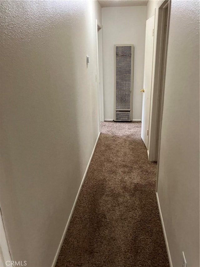 corridor with baseboards, a heating unit, and carpet floors