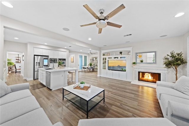 living area with recessed lighting, visible vents, light wood-style floors, and a warm lit fireplace