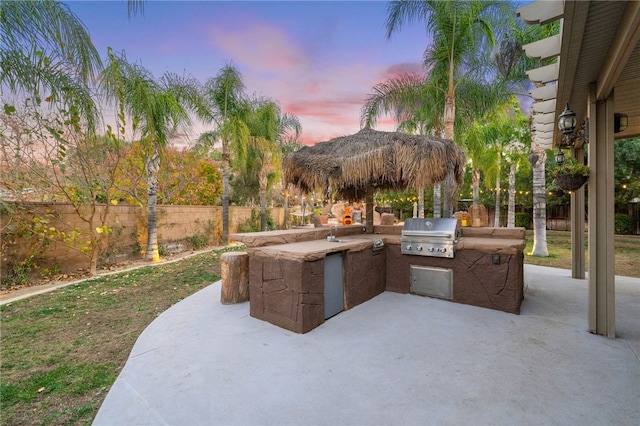 patio terrace at dusk with area for grilling, fence, and a grill