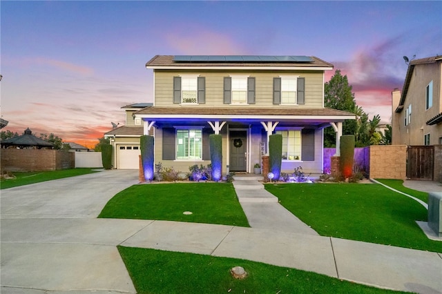 view of front of house with concrete driveway, a yard, fence, and roof mounted solar panels