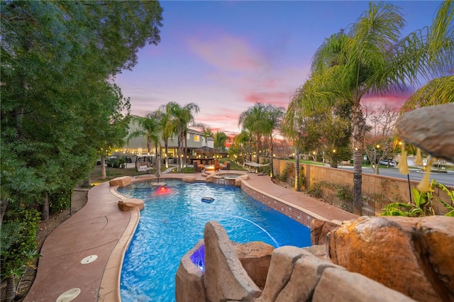 pool at dusk with a patio area and a pool with connected hot tub