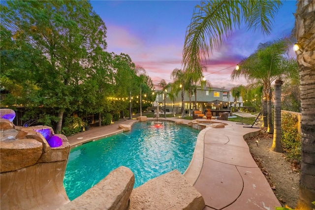 pool at dusk with an outdoor pool and a patio