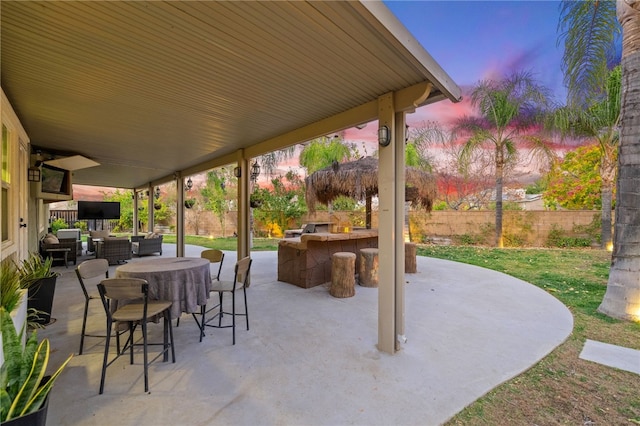 patio terrace at dusk with outdoor dining area, fence, and outdoor dry bar