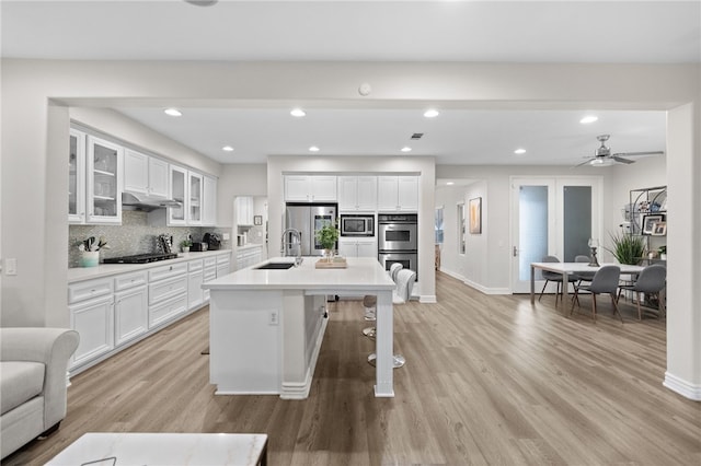 11119 Iris Ct, Corona, CA 92883 - kitchen featuring appliances with stainless steel finishes, white cabinetry, under cabinet range hood, light wood finished floors, and recessed lighting