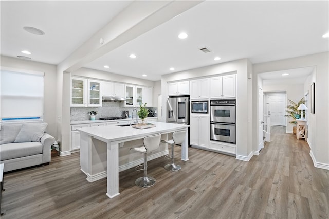 kitchen with visible vents, backsplash, appliances with stainless steel finishes, a kitchen breakfast bar, and light wood-style floors