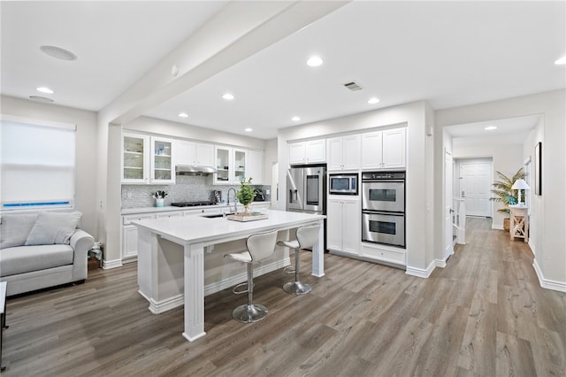 11119 Iris Ct, Corona, CA 92883 - kitchen featuring appliances with stainless steel finishes, light wood finished floors, a breakfast bar area, white cabinets, and glass insert cabinets