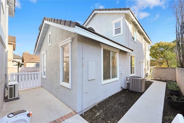 view of side of property with central AC unit, fence, stucco siding, ac unit, and a patio area