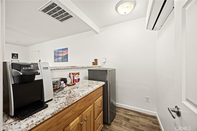 kitchen featuring visible vents, brown cabinets, dark wood finished floors, a wall unit AC, and light stone countertops