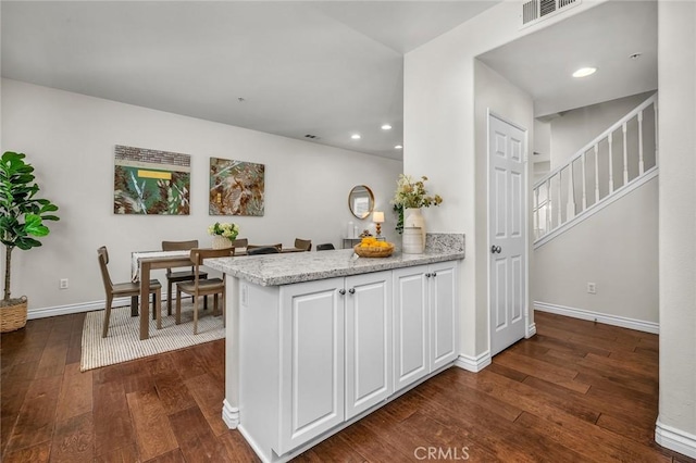 kitchen with visible vents, light stone counters, dark wood finished floors, white cabinetry, and baseboards