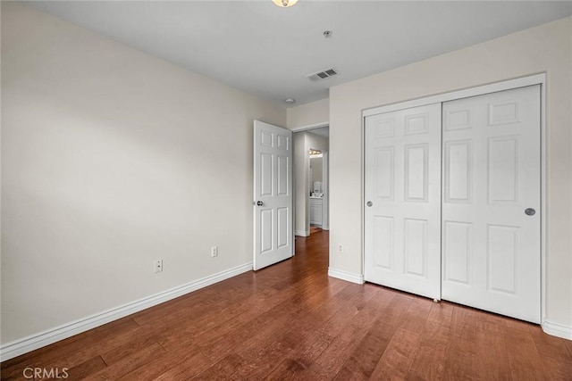 unfurnished bedroom with visible vents, baseboards, a closet, and wood finished floors