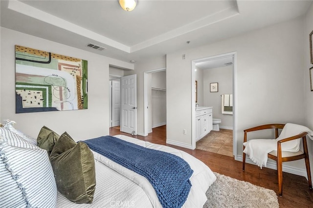 bedroom with visible vents, a raised ceiling, baseboards, and wood finished floors