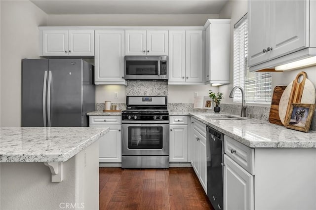 kitchen with light stone countertops, dark wood finished floors, a sink, appliances with stainless steel finishes, and white cabinetry